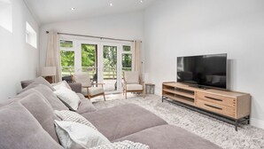 A modern living room with a large flat-screen TV, a sofa set, and a dining area with chairs. - Orchard View Cottage | Escape Ordinary (Derrygonnelly)