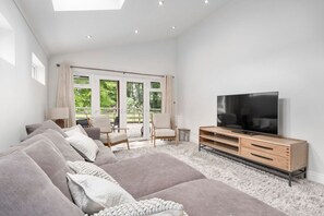 A modern living room with a large flat-screen TV, a sofa set, and a dining area with chairs. - Orchard View Cottage | Escape Ordinary (Derrygonnelly)