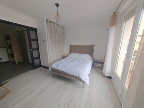 Quarto com cama, luminária no teto, uma porta e vista pela janela.