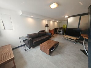 Uma sala de estar moderna com sofá, mesa de centro, TV e um espaço de jantar com cadeiras.