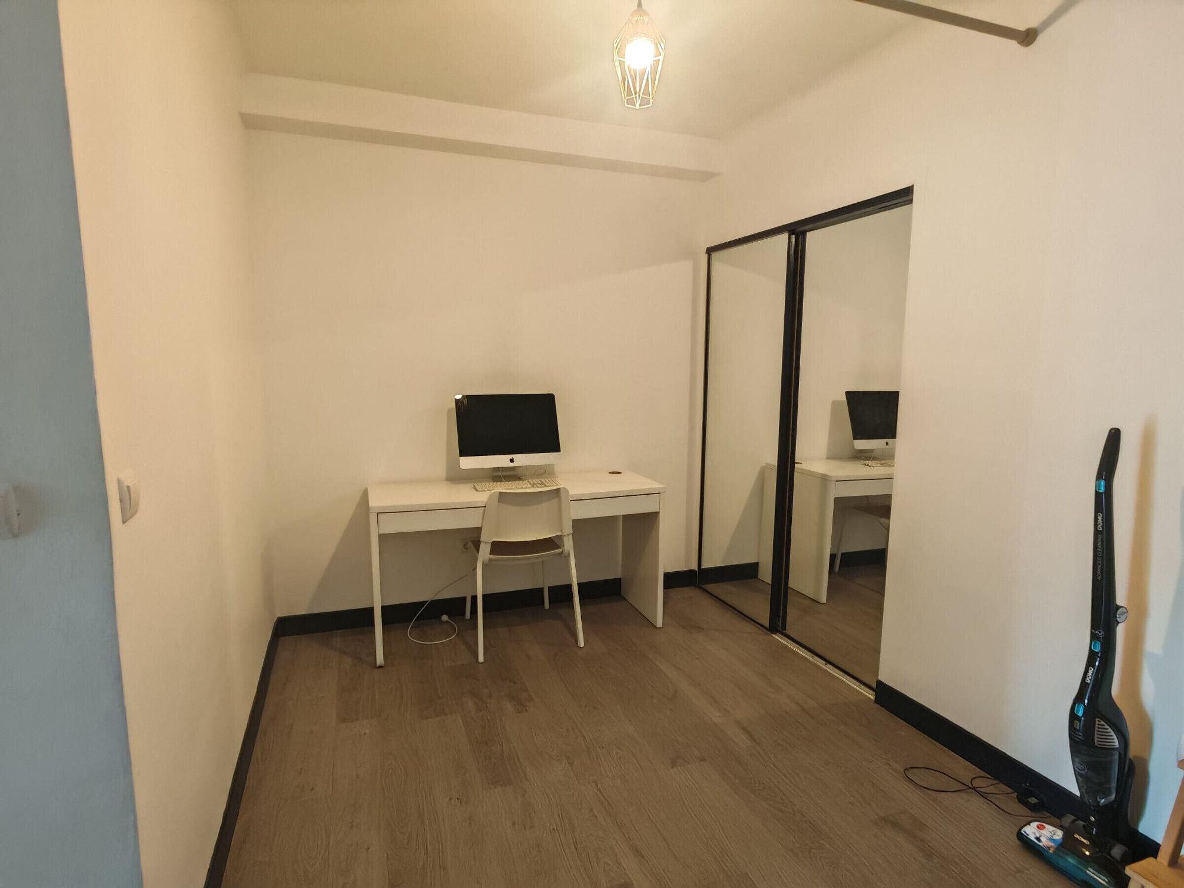 A room with a white desk, a chair, a computer, and a large mirror.