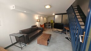 Ein Wohnzimmer mit Sofa, Couchtisch, Fernseher und einer Treppe.