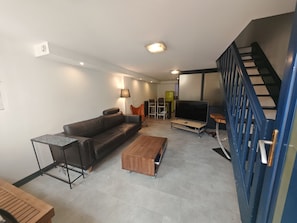 Uma sala de estar com sofá, mesa de centro, TV e escada.