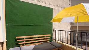 Ein Balkon mit einer hölzernen Bank und einem gelben Sonnenschirm.