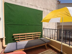 Uma varanda com um banco de madeira e um guarda-sol amarelo.