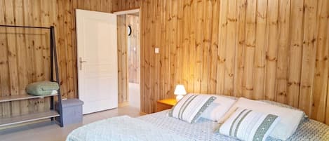 Una habitación con paredes de paneles de madera, una cama con ropa de cama estampada, una mesita de noche con una lámpara y un banco con cojín.