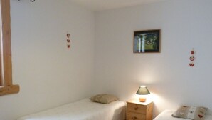 Una habitación pequeña y sencilla con dos camas individuales, una mesita de noche con lámpara y un cuadro enmarcado en la pared.
