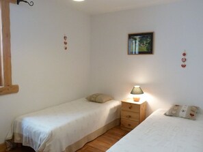 Ein kleiner, einfacher Raum mit zwei Einzelbetten, einem Nachttisch mit Lampe und einem gerahmten Bild an der Wand.