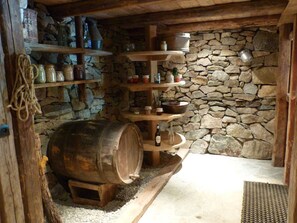 Eine rustikale Küche mit Steinwänden, Holzböden und Regalen, einem großen Fass und diversen Küchenutensilien.