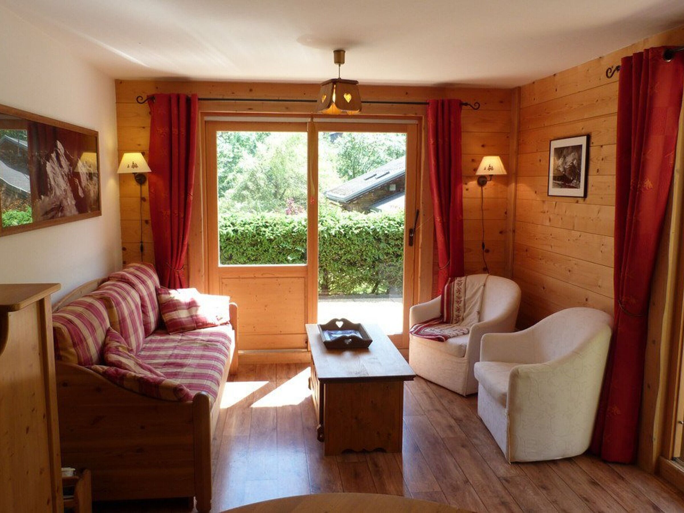 A cozy room with a wooden floor, a striped sofa, a white armchair, a small table, and a window with curtains.