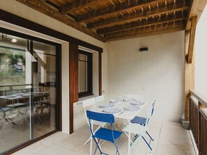Eine Terrasse mit Tisch für vier Personen, umgeben von blauen und weißen Stühlen, unter einer Holzbeschichtung.
