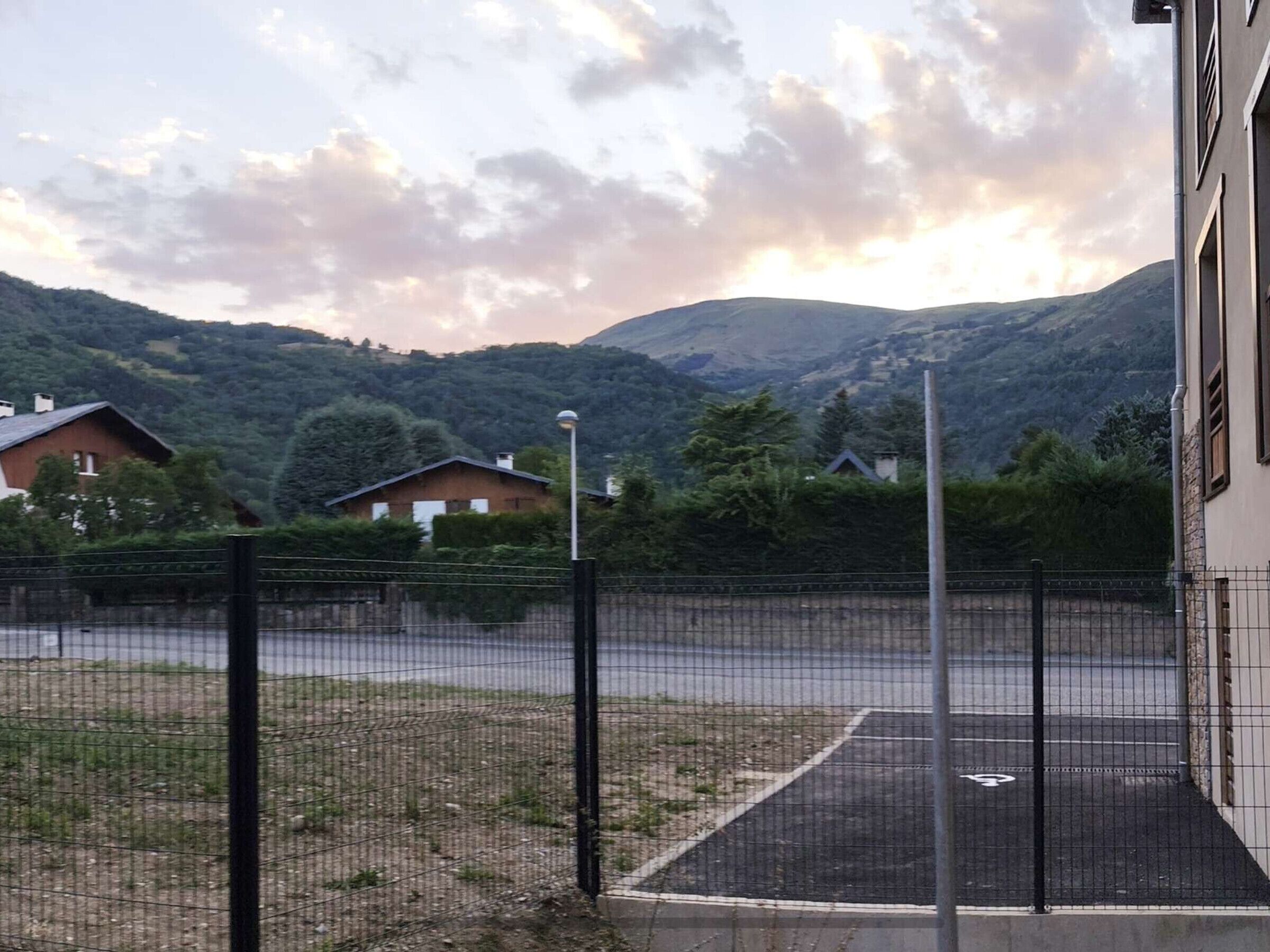 A fenced parking area with a view of a mountain range and houses in the background.