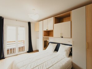 A bedroom with a bed, a wardrobe, a ceiling light, and a window with curtains. - Modern apartment - 4 guests - Saint-Lary (Saint-Lary-Soulan)