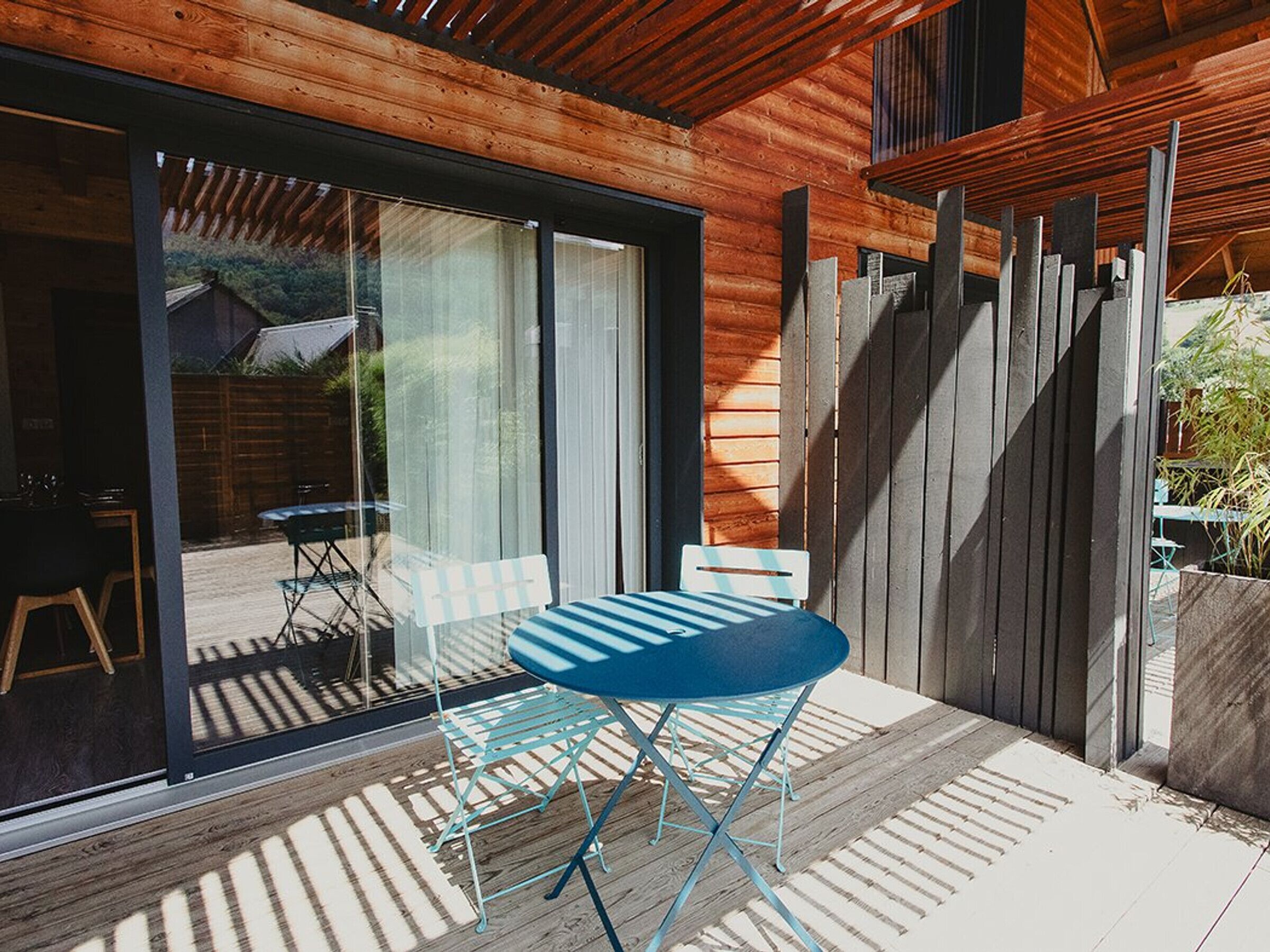 Une terrasse avec une table et des chaises, une plateforme en bois et une porte-fenêtre coulissante donnant sur un espace extérieur.