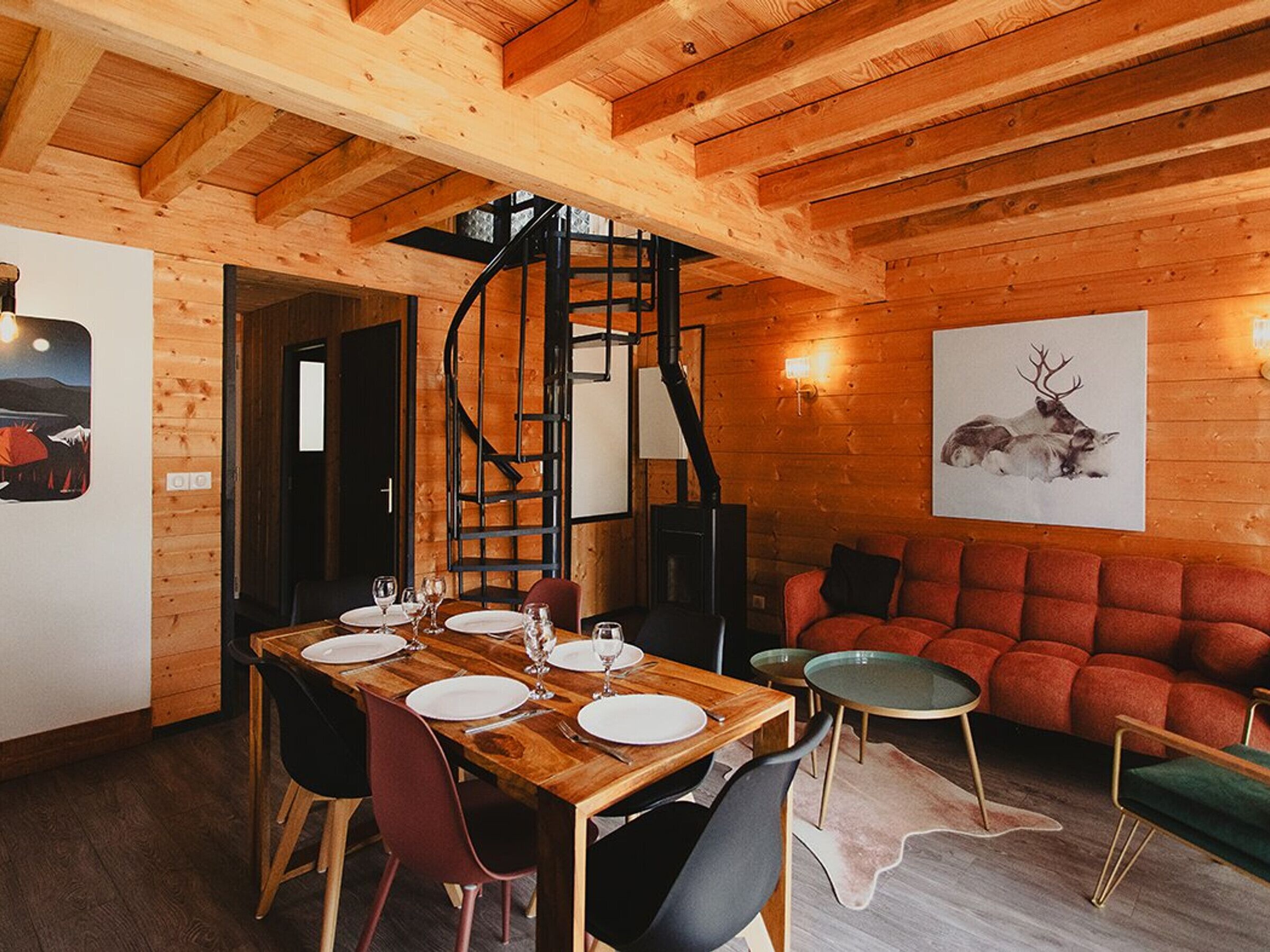 Interior de madera con una mesa de comedor para cuatro, una escalera en espiral y un sofá rojo.