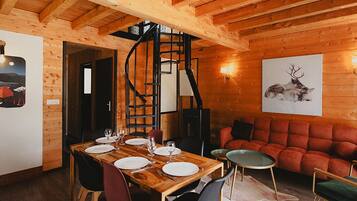 A wooden interior with a dining table set for four, a spiral staircase, and a red sofa.