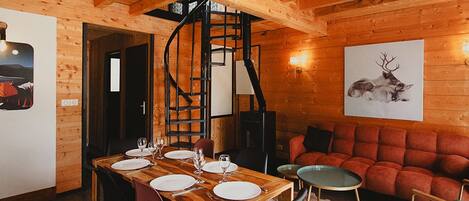 Interior de madera con una mesa de comedor para cuatro, una escalera en espiral y un sofá rojo.