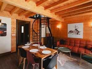Interior de madeira com uma mesa de jantar posta para quatro pessoas, uma escada em espiral e um sofá vermelho.