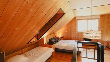 A cozy attic bedroom with wooden walls, a sloped ceiling, a chandelier, and two beds.
