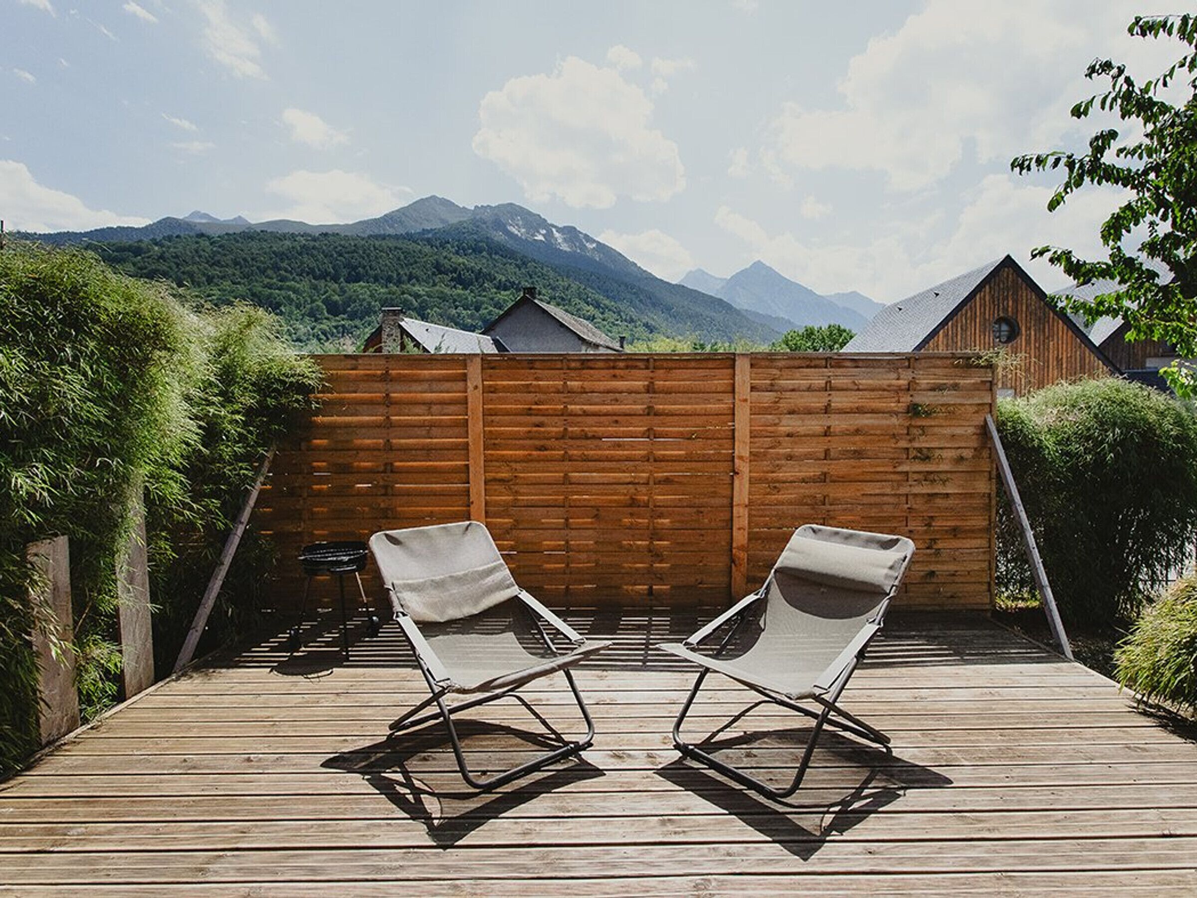 Terraza de madera con dos sillones de relax orientados hacia una valla de madera, con vistas a un paisaje montañoso.