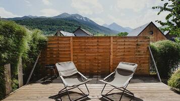 Terraza de madera con dos sillones de relax orientados hacia una valla de madera, con vistas a un paisaje montañoso.
