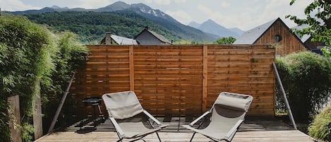 A wooden deck with two lounge chairs facing a wooden fence, overlooking a mountainous landscape.