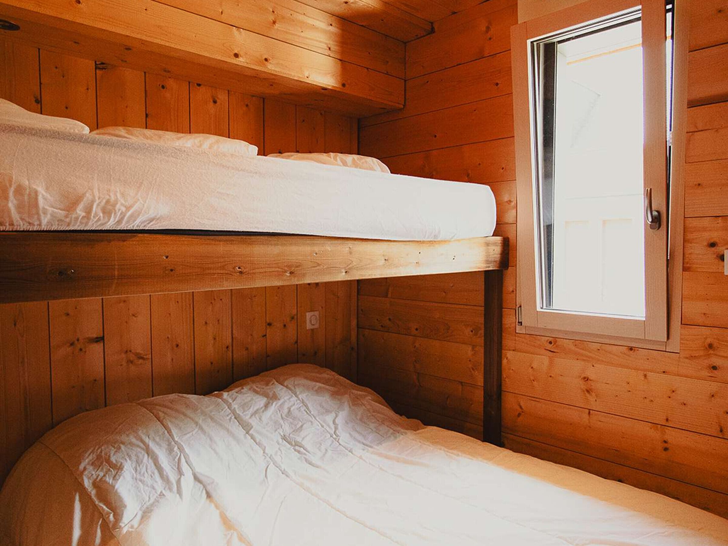 Une chambre avec un lit superposé, des murs en bois et une fenêtre.