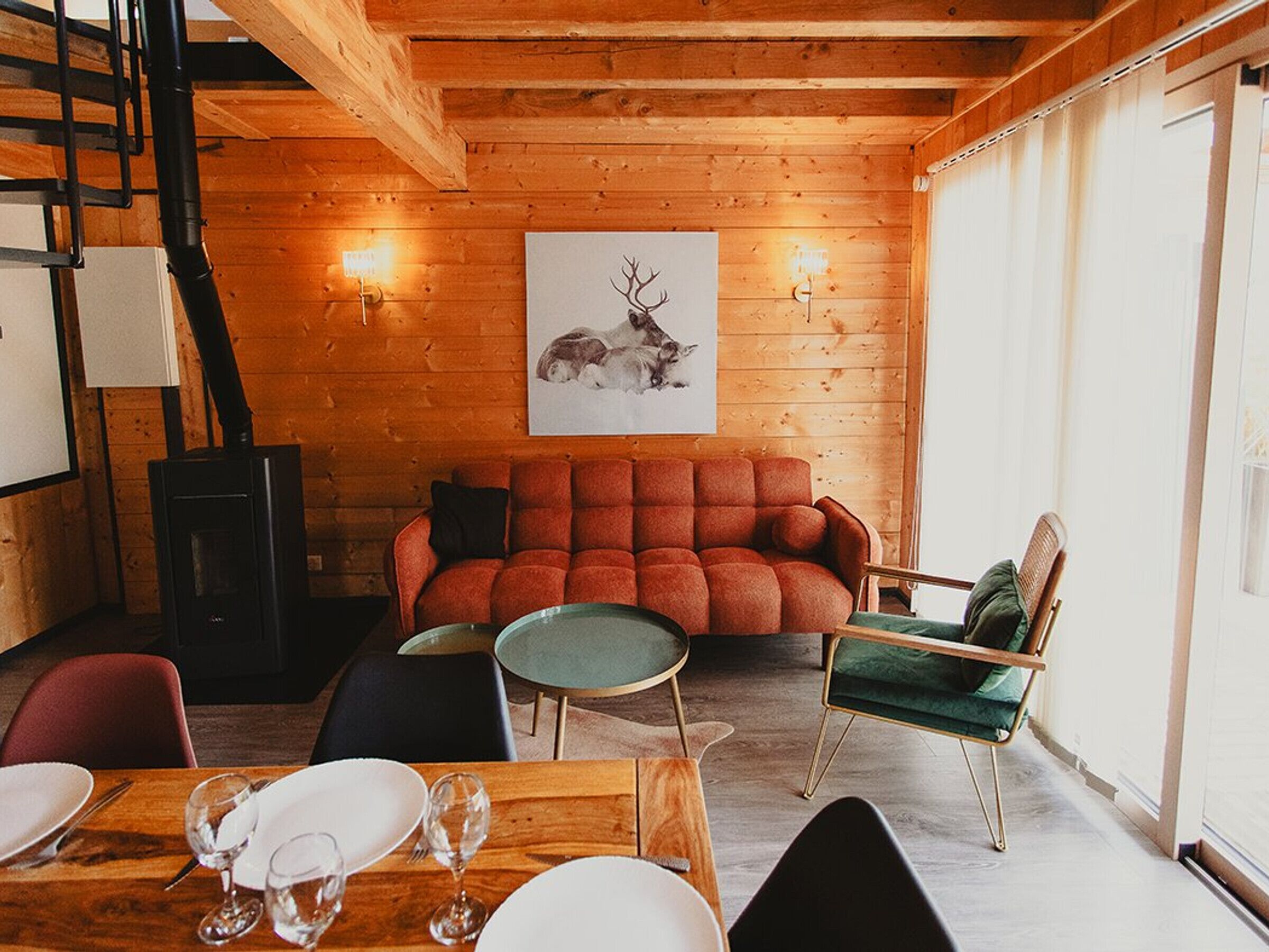 Una habitación acogedora con techo de madera, un sofá rojo, una silla verde y una mesa de comedor con platos y vasos.