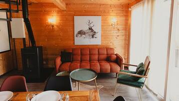 Una habitación acogedora con techo de madera, un sofá rojo, una silla verde y una mesa de comedor con platos y vasos.
