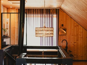 A room with a hanging chandelier, wooden walls, a window with vertical blinds, and a visible staircase. - Charming apartment in Sailhan - 6 guests (SAILHAN)