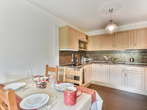 Une cuisine moderne avec des meubles en bois, une table à manger pour quatre personnes et un luminaire suspendu.