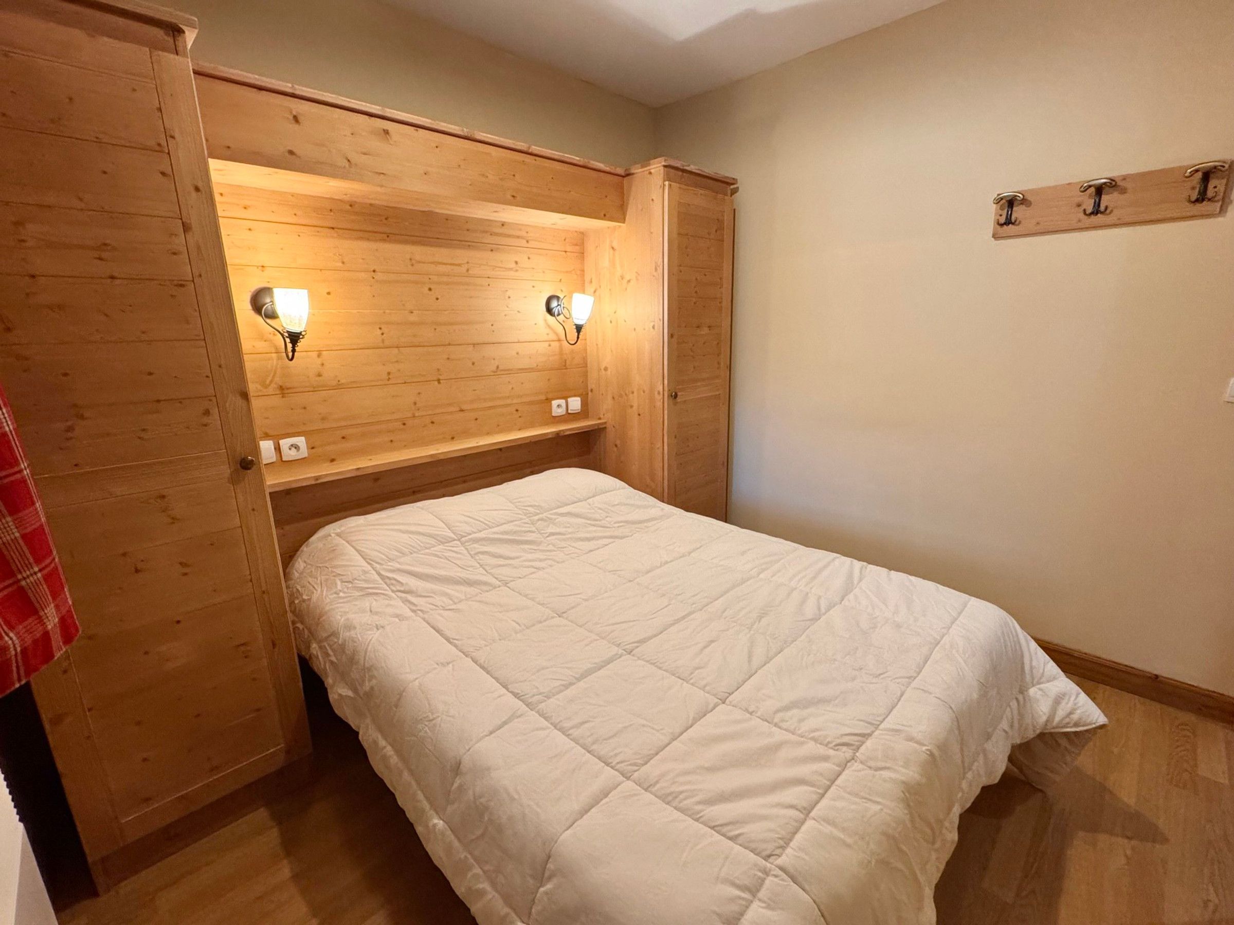 Une chambre à coucher avec un lit, une tête de lit en bois, deux lampes fixées au mur et une étagère en bois.