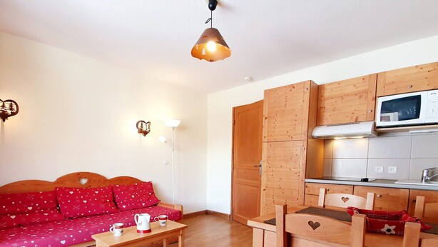 A compact living space with a wooden sofa, a small wooden table, a kitchenette with a microwave, and a hanging pendant light. - Apartment pets, mountain view - 4 guests (Vars)
