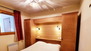 A bedroom with a bed, wooden headboard, bedside lamps, a window with curtains, and a ceiling light fixture. - Apartment pets, mountain view - 4 guests (Vars)