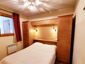 Ein Schlafzimmer mit einem Bett, einem Holzkopfstück, Nachttischlampen, einem Fenster mit Vorhängen und einer Deckenleuchte.