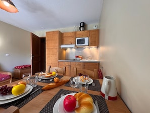 A dining area with a wooden table set for a meal, a kitchen with wooden cabinets and a microwave, and a red chair visible in the background. - Apartment pets, mountain view - 4 guests (Vars)