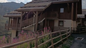 A wooden chalet with a balcony and stairs, surrounded by a wooden fence and flowering plants. - Apartment pets, mountain view - 4 guests (Vars)