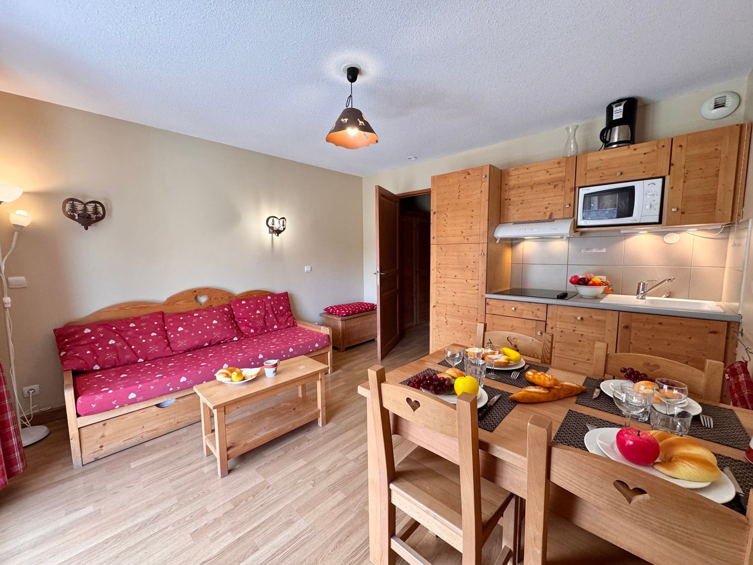 A compact living space with a kitchenette, a dining table set with food, and a sofa with a heart-patterned cover.