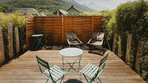 Eine Holzterrasse mit Tisch und Stühlen, umgeben von einem Holenzaun, mit einer bergigen Landschaft im Hintergrund.