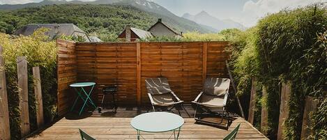 A wooden deck with a table and chairs, surrounded by a wooden fence, with a mountainous landscape in the background.