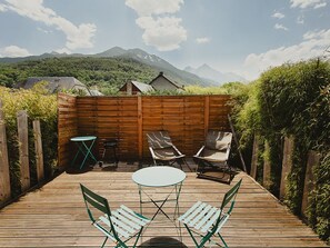 Eine Holzterrasse mit Tisch und Stühlen, umgeben von einem Holenzaun, mit einer bergigen Landschaft im Hintergrund.