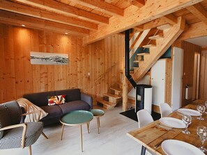 A wooden interior with a sofa, dining table, chairs, and a staircase.
