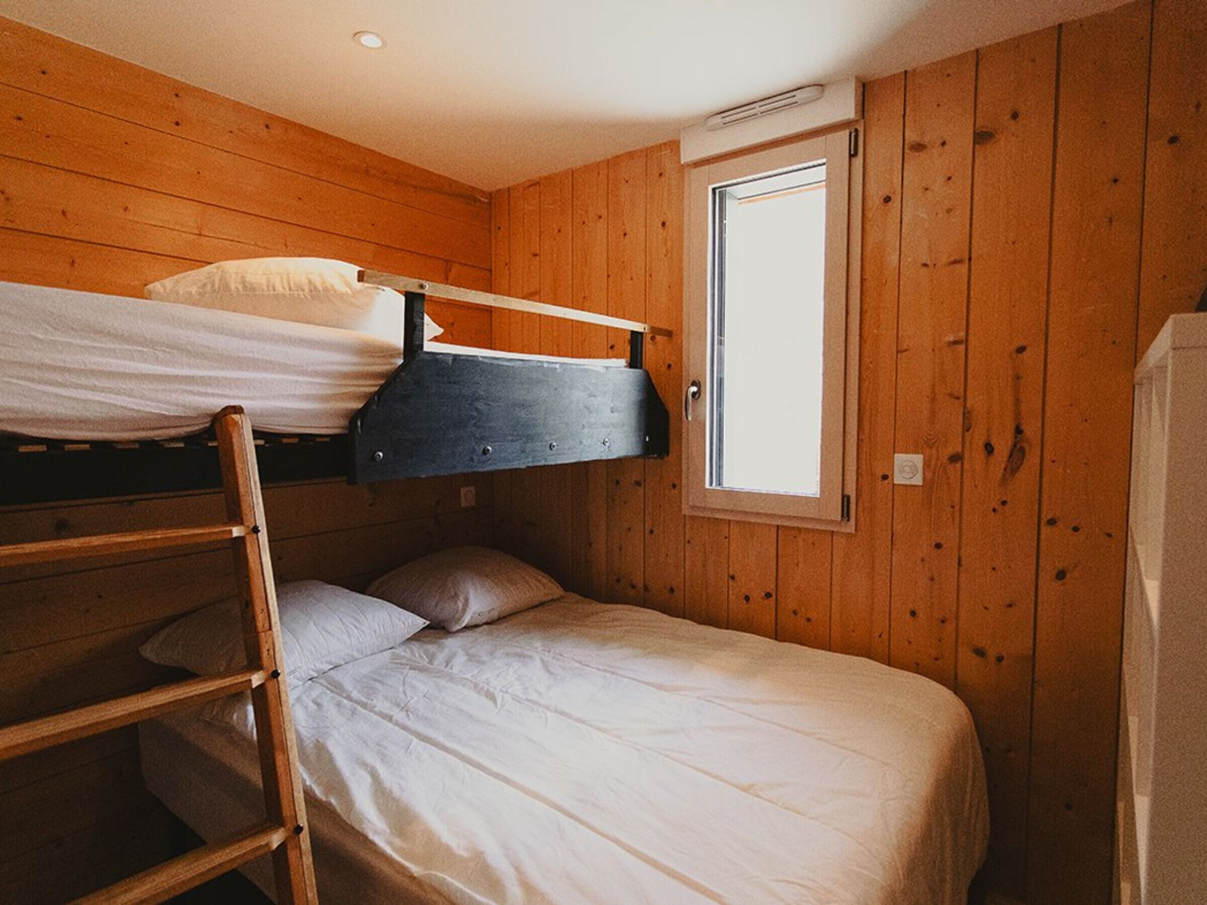 Habitación con literas, paredes de madera, una ventana y una escalera.