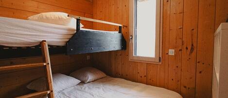 Habitación con literas, paredes de madera, una ventana y una escalera.