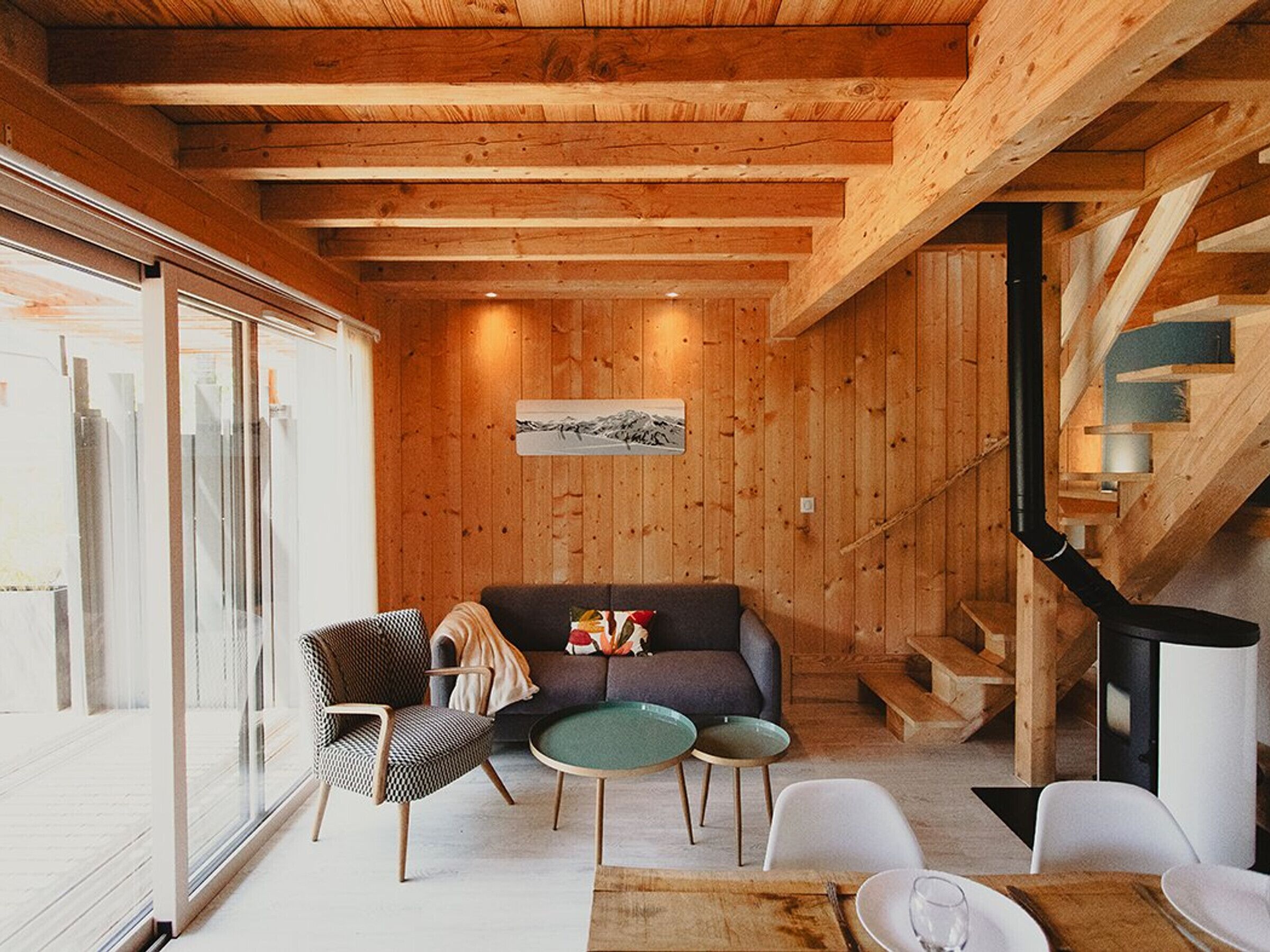 Een gezellig interieur van een chalet met houten plafond, een bank, een eettafel en een open haard.