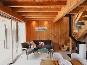 A cozy cabin interior with a wooden ceiling, a sofa, a dining table, and a fireplace.