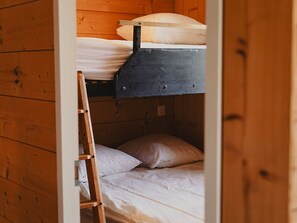 Cama litera con escalera, paredes de madera y colchón blanco.