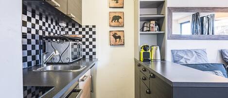 A compact kitchen with a checkered backsplash, a built-in oven, and a microwave. There are three wooden wall art pieces depicting animals.