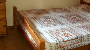 A bed with a patterned bedspread and wooden headboard in a room with wooden walls and a dresser. - Cosy 2-Room Mezzanine Apartment, Sleeps 5, South-Facing Balcony, Near Linga Lift, Parking Included (Châtel)