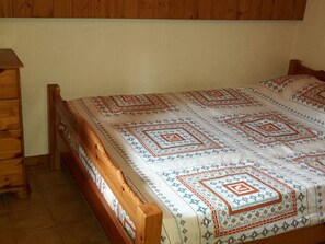 A bed with a patterned bedspread and wooden headboard in a room with wooden walls and a dresser. - Cosy 2-Room Mezzanine Apartment, Sleeps 5, South-Facing Balcony, Near Linga Lift, Parking Included (Châtel)